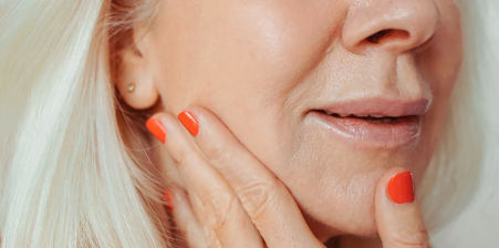 Up close image of an older lady with red nails touching her skin